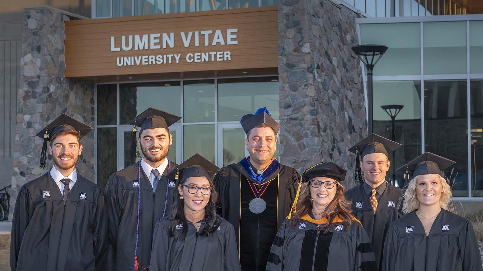 University of Mary graduates standing outside the Lumen Vitae University Center with President Monsignor James Shea.