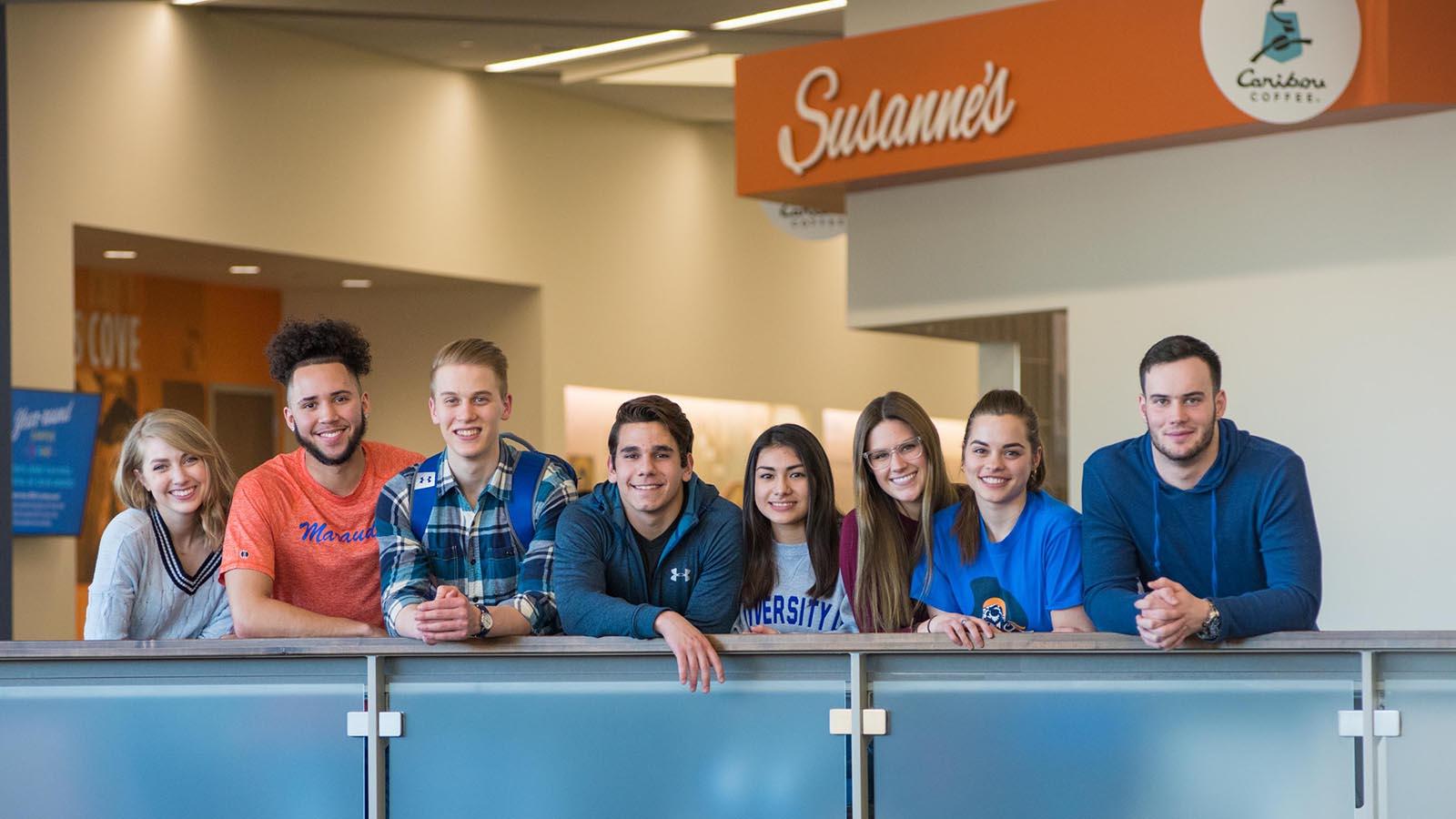 Eight University of Mary students smiling and overlooking balcony in the Lumen Vitae University Center