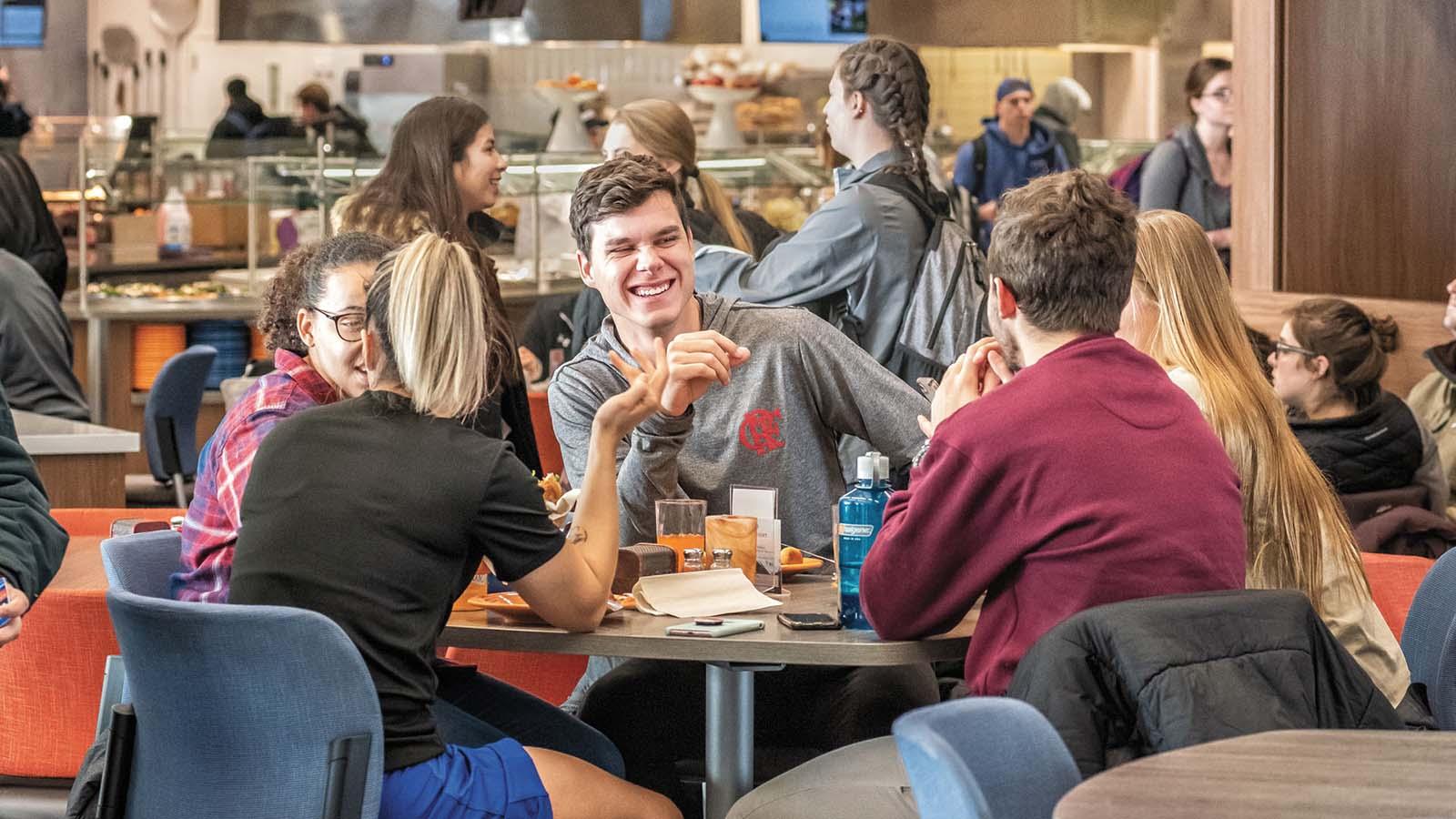 Group of students eating a meal together and laughing in the Crow’s Nest Campus Restaurant