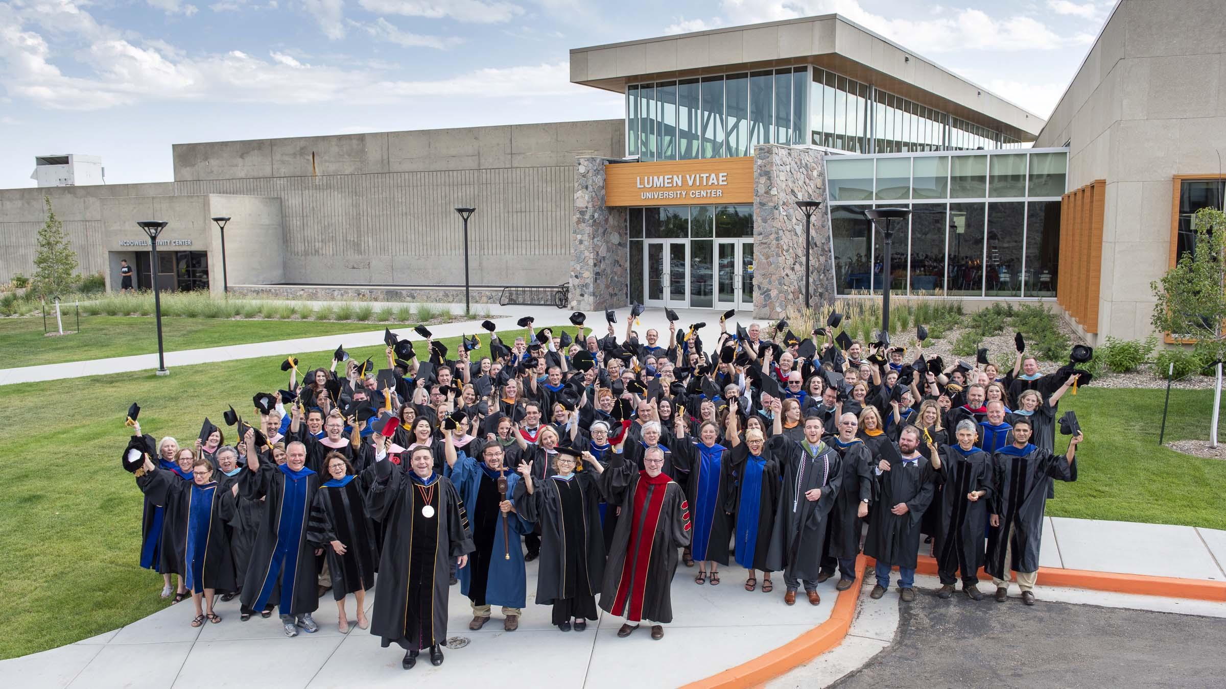 Faculty, staff and Monsignor James P. Shea in their graduation robes, holding graduation caps.