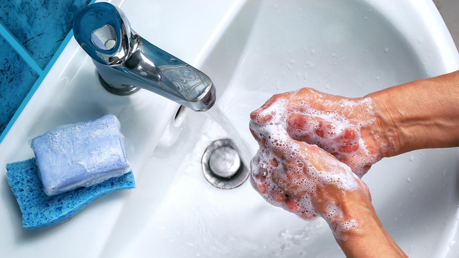 Soapy hand over the sink and piece of blue soap.