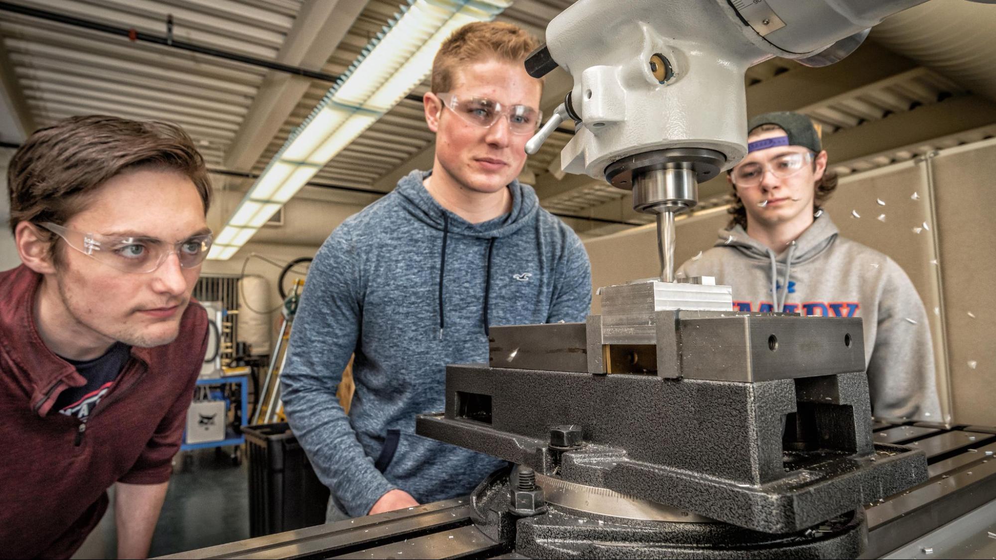 Three engineering students work together to operate a drill saw