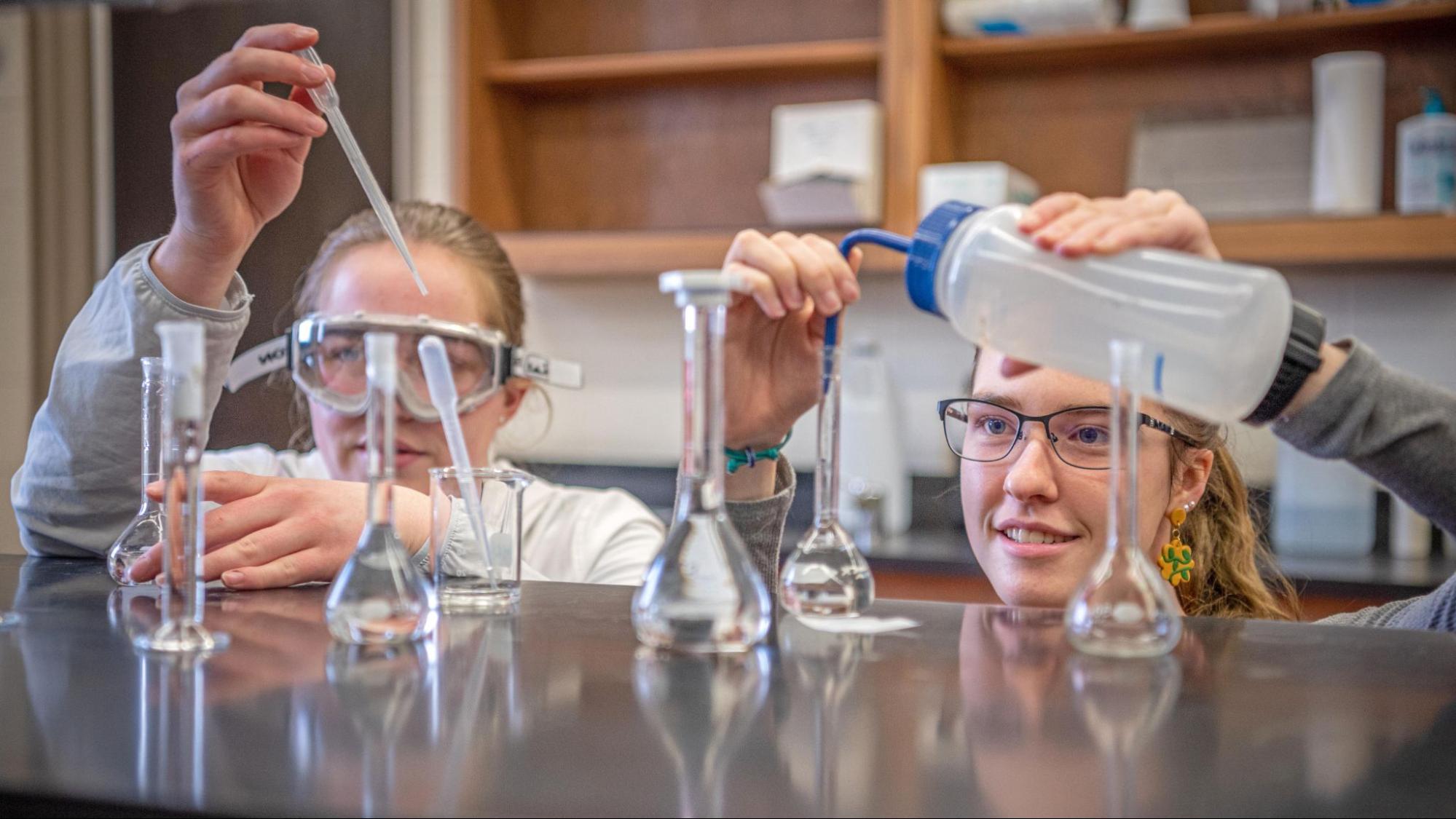 Two students dropping chemicals into glass beakers.
