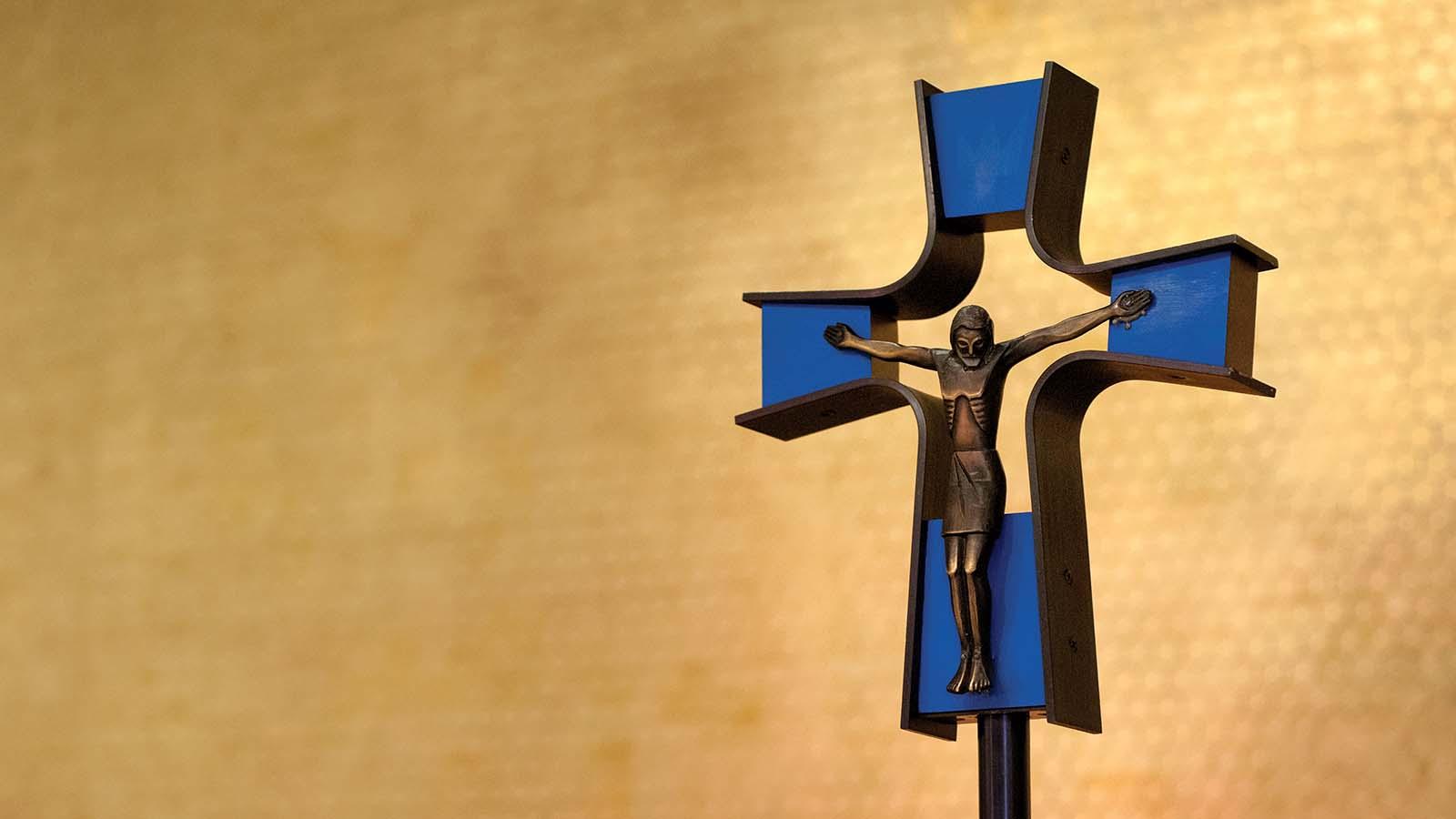 Closeup of crucifix in front of gold-leafed wall.