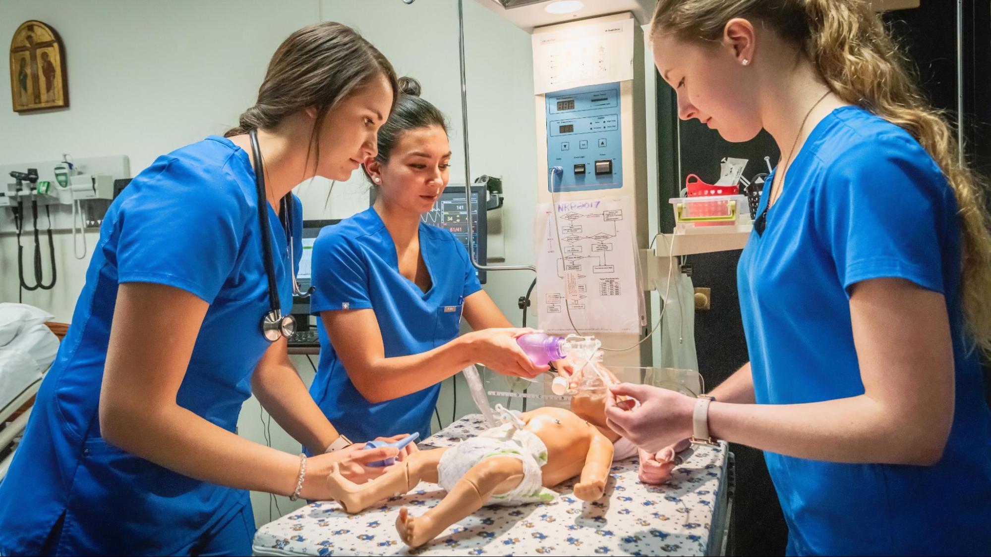 Three student nurses giving oxygen to a synthetic baby.