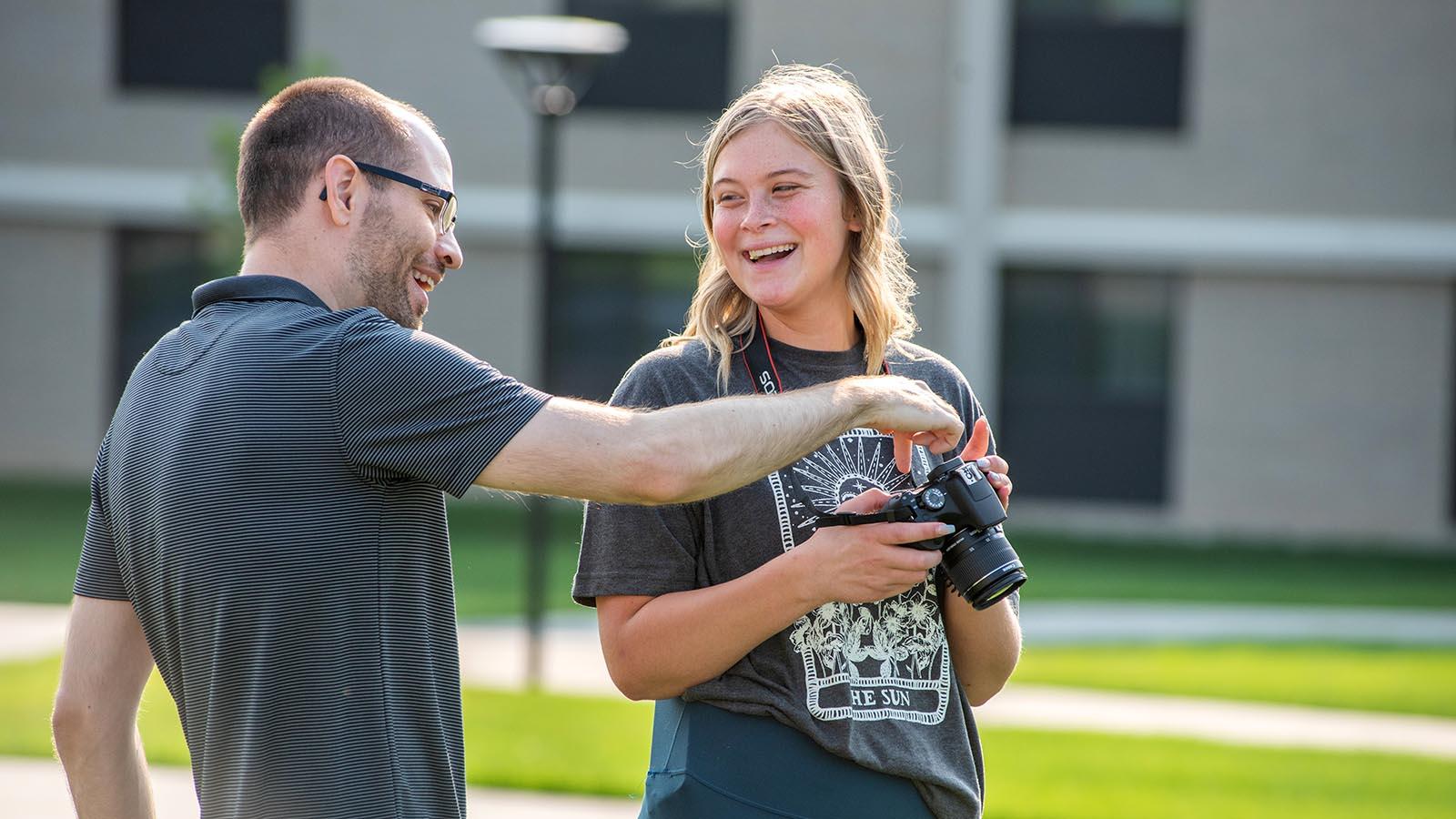 Photography professor smiling and pointing to controls on year-round campus student’s camera