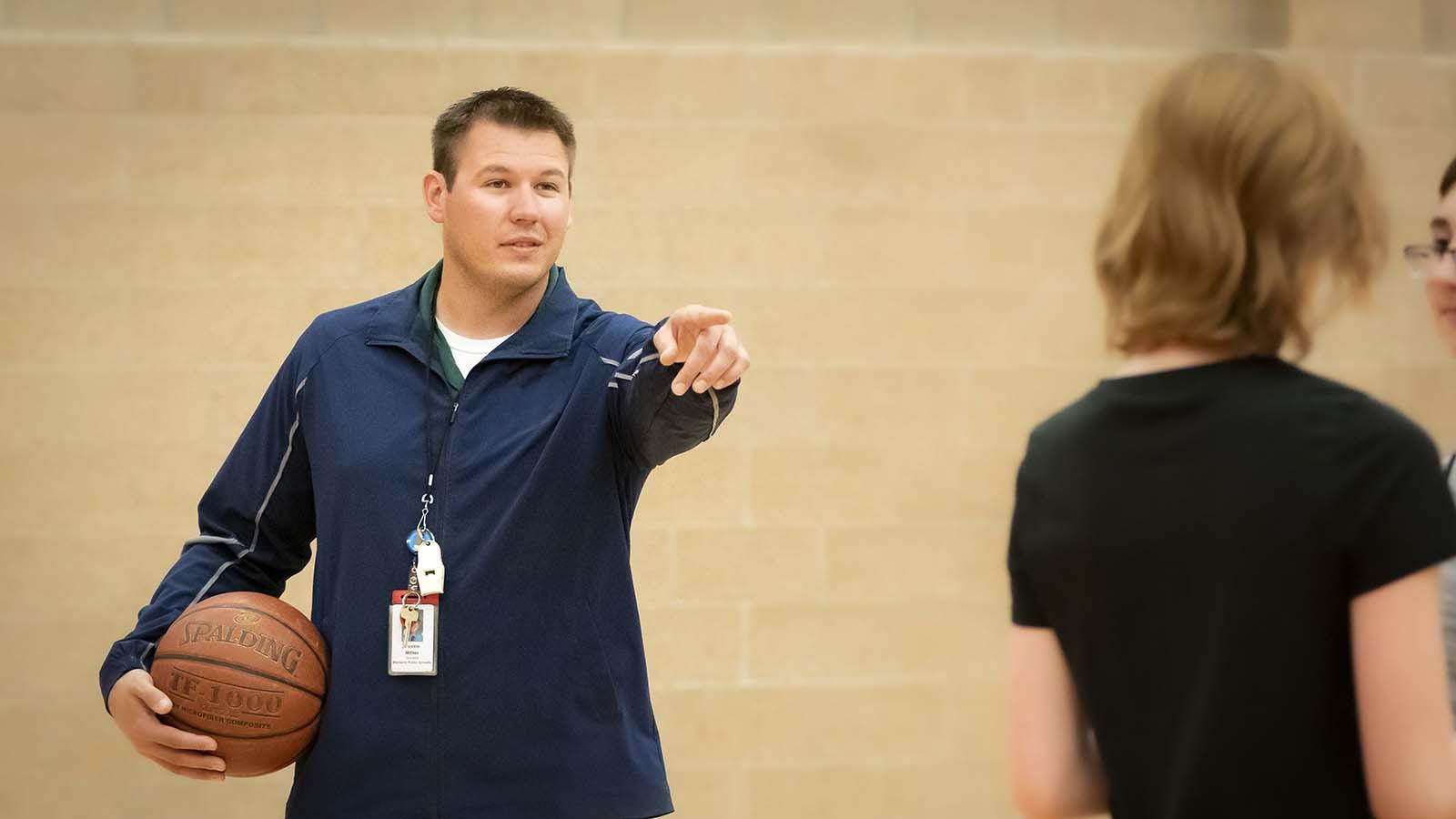 Physical education teacher teaching basketball to high school students