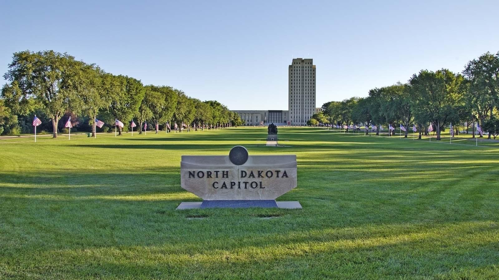 Alt text: A concrete sign for the ND State Capitol is in forefront with the expansive lawn and capitol building in the background. 