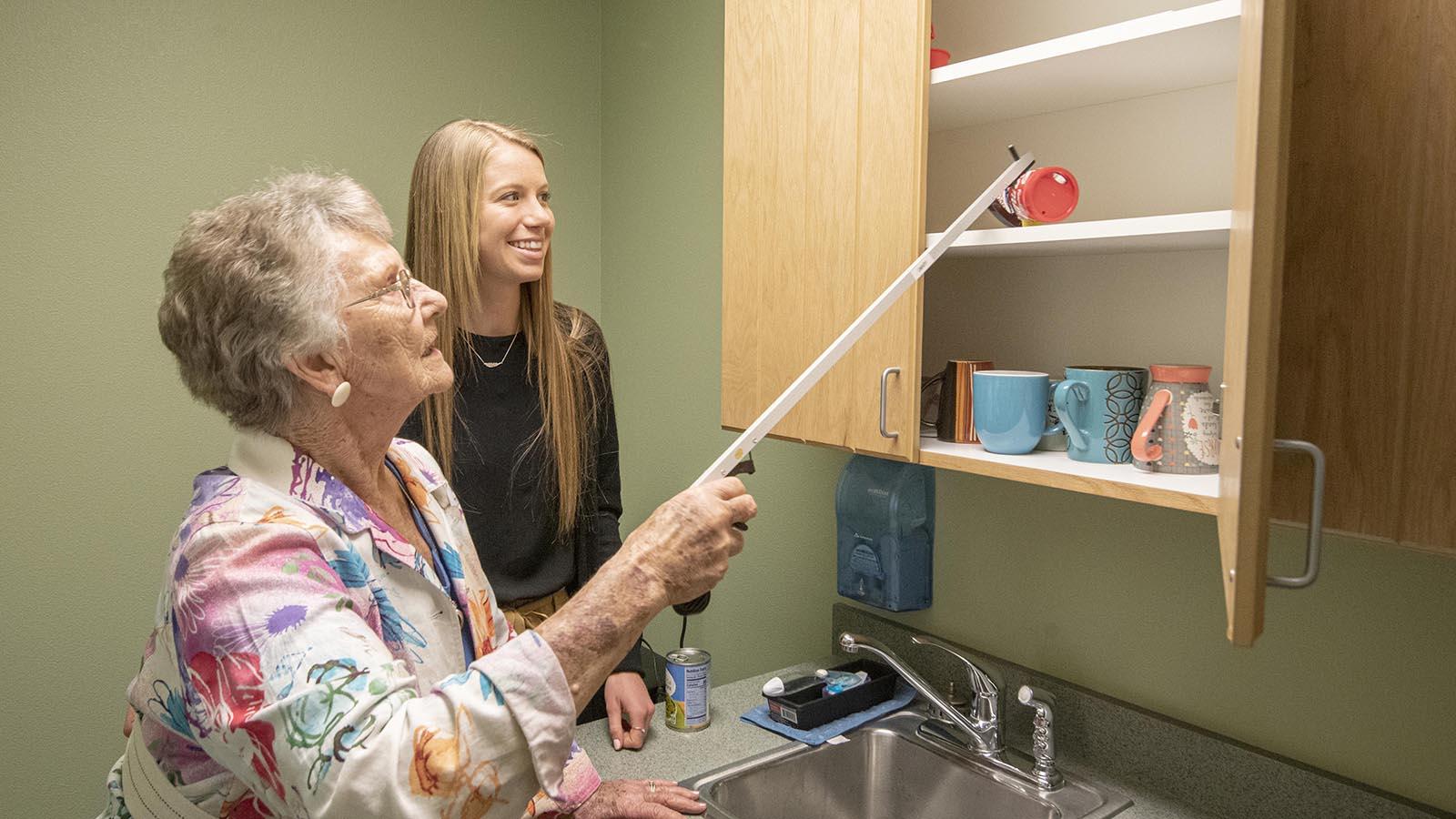 Occupational therapy doctoral student teaching an elderly client how to grab items from the cupboard