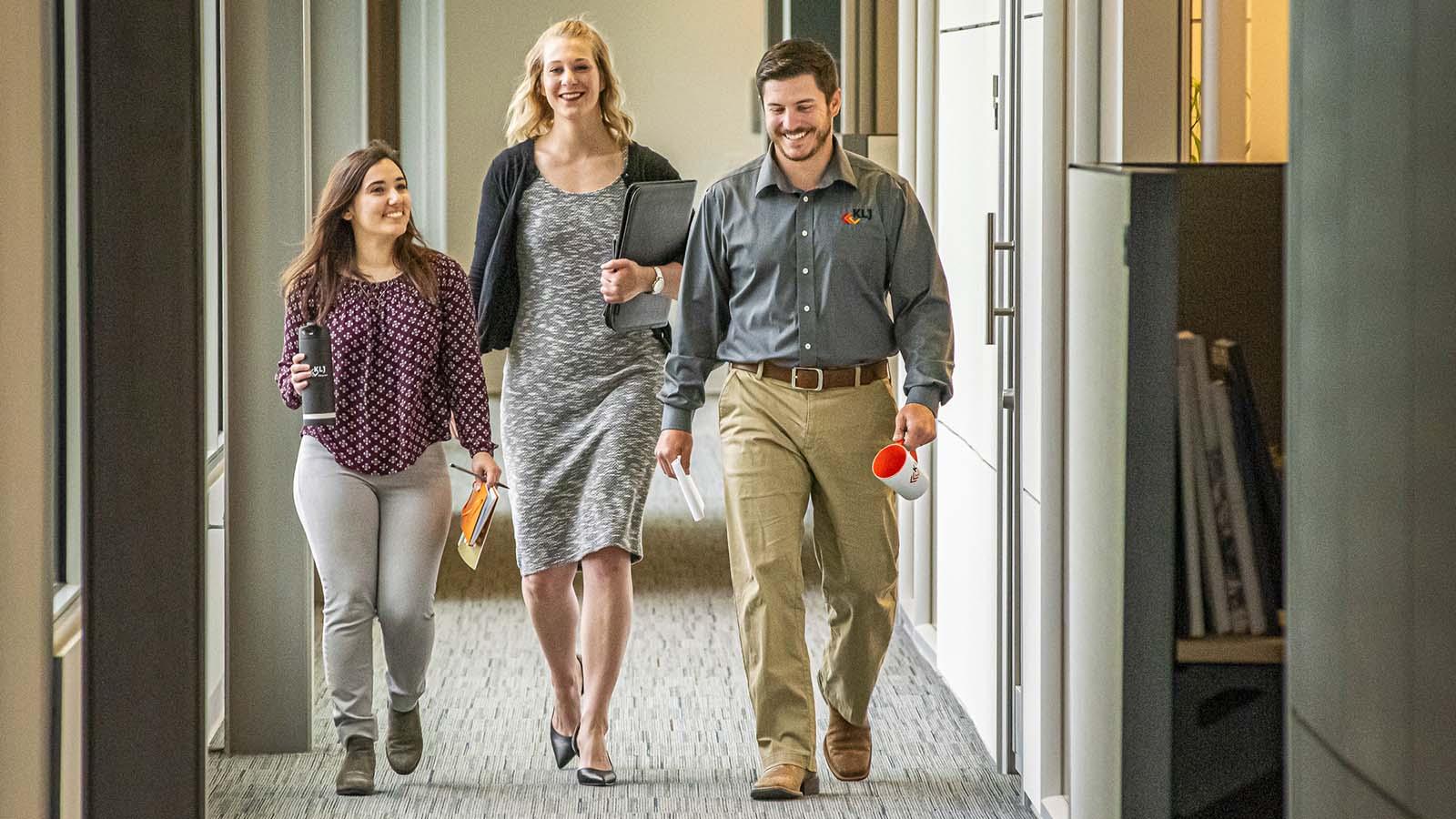 Three smiling alumni walking down a hallway at business