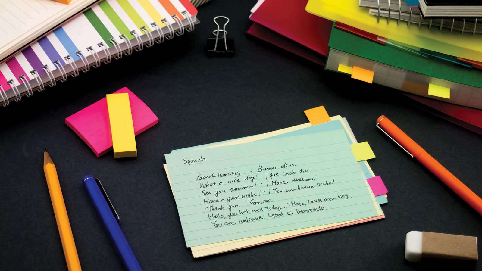 Notebooks, folders, and pens on desk with notecards that have English to Spanish translations