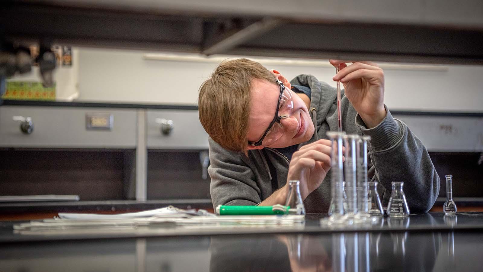 Male student with protective goggles adding chemicals to a beaker