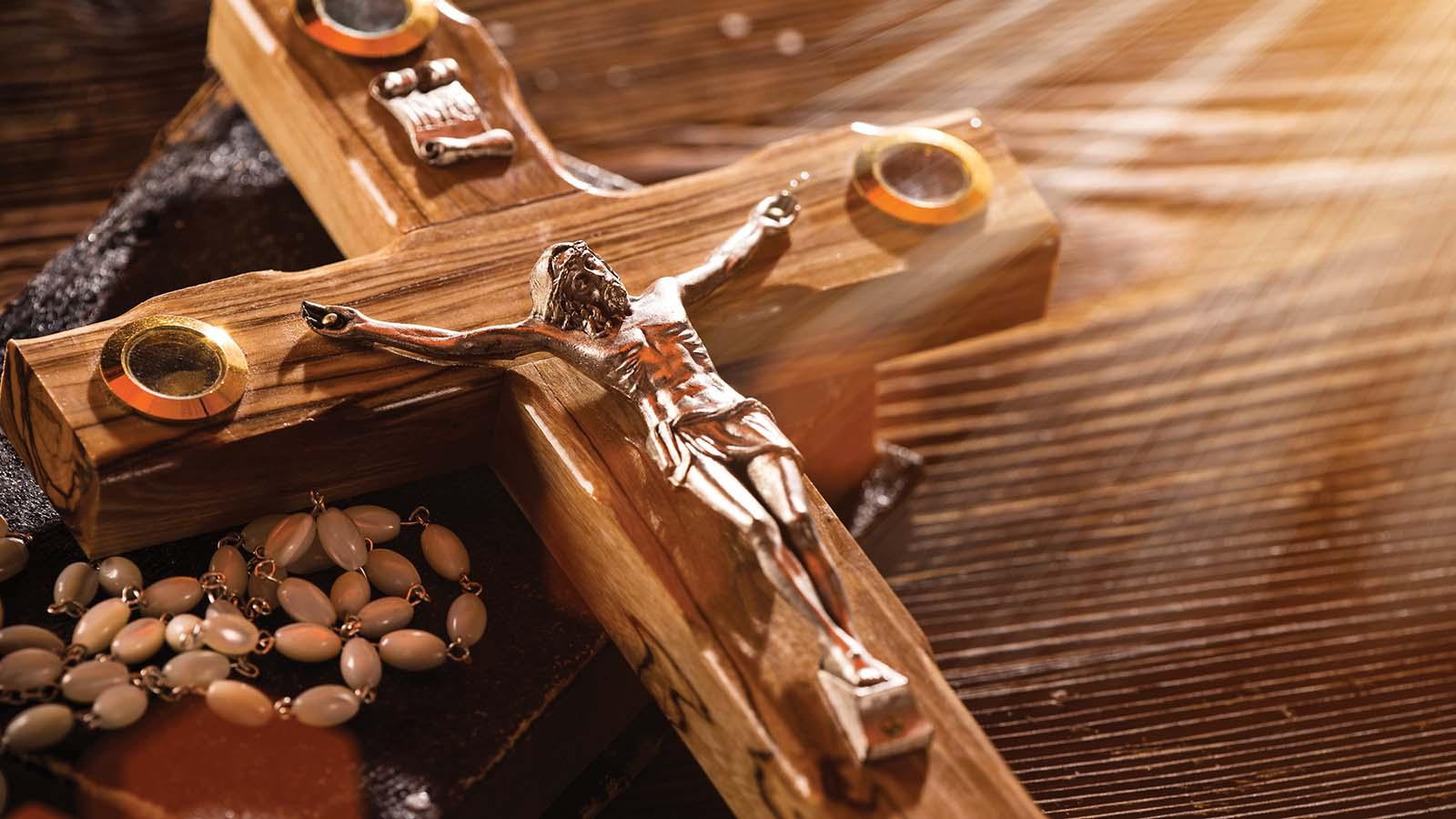 Sunlight shining on wooden crucifix and rosary setting on a wood table 