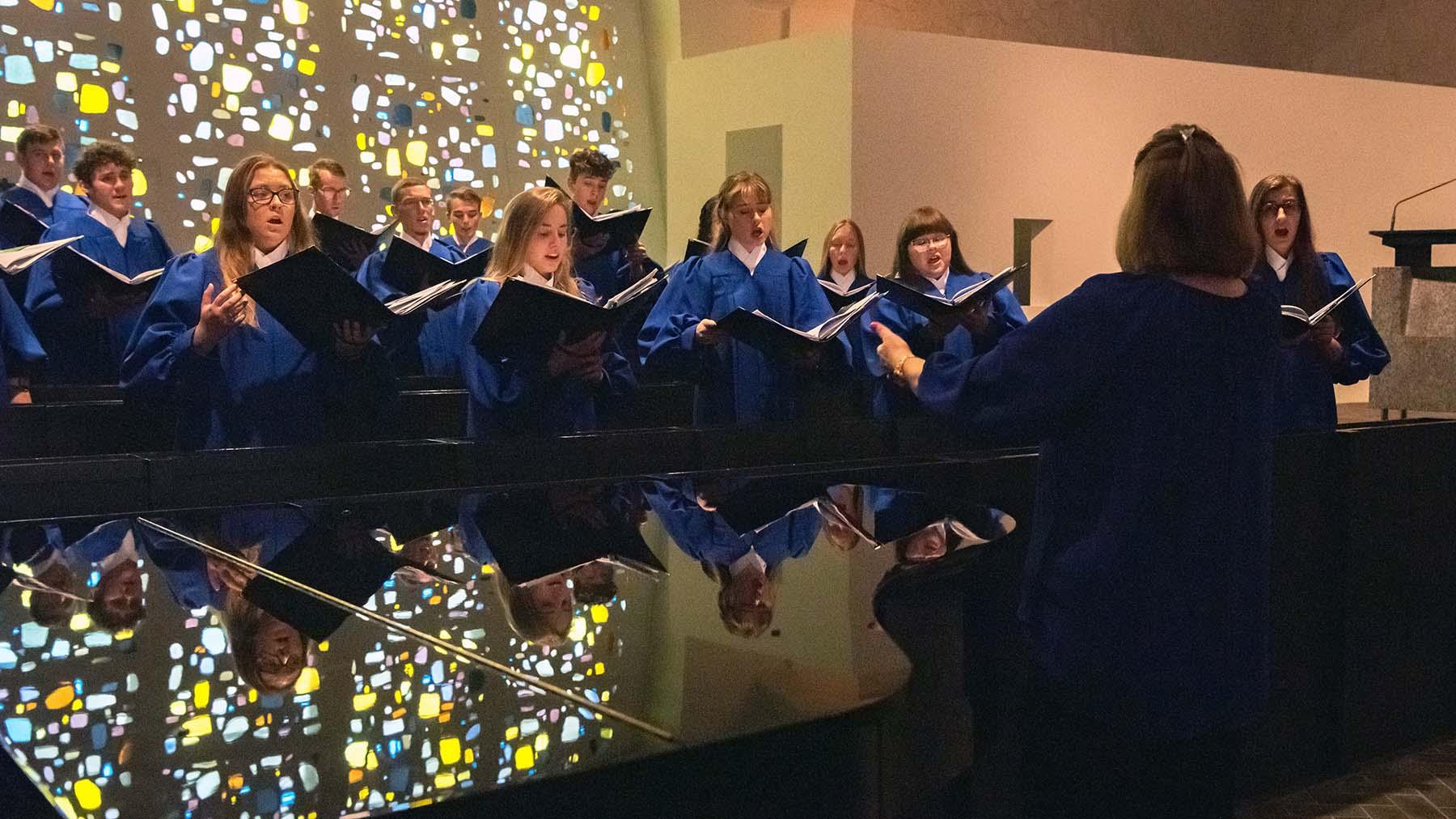 Choir singing in front of stained glass windows with conductor in front