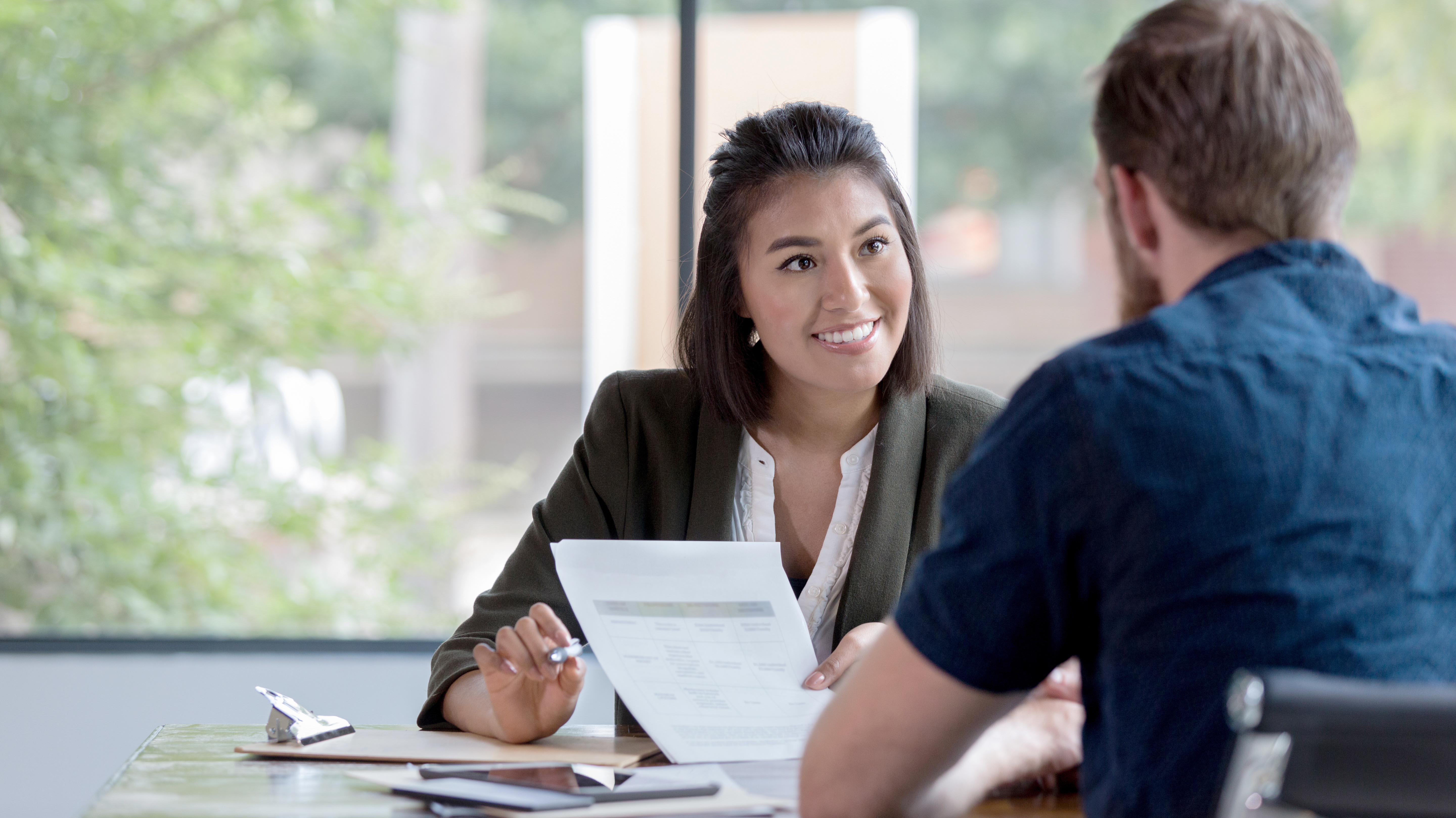 Female banker smiles while showing a document to a male customer