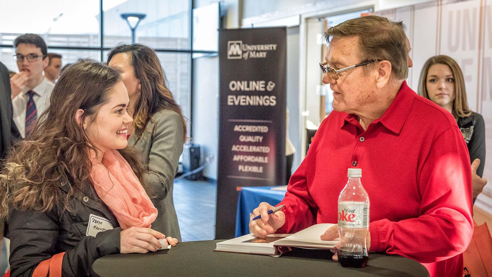 Smiling business student talking with Gary Tharaldson as he signs a copy of Open Secrets of Success