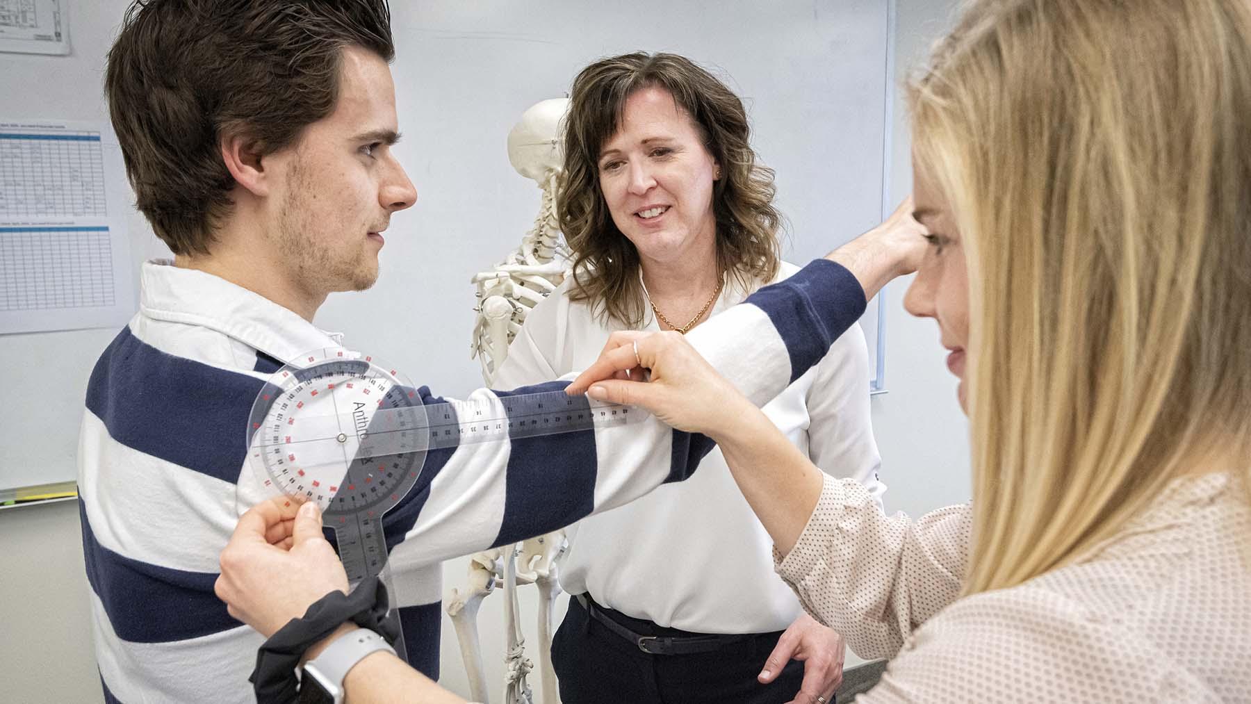 Occupational therapy student assessing shoulder movement of a classmate with the professor looking on