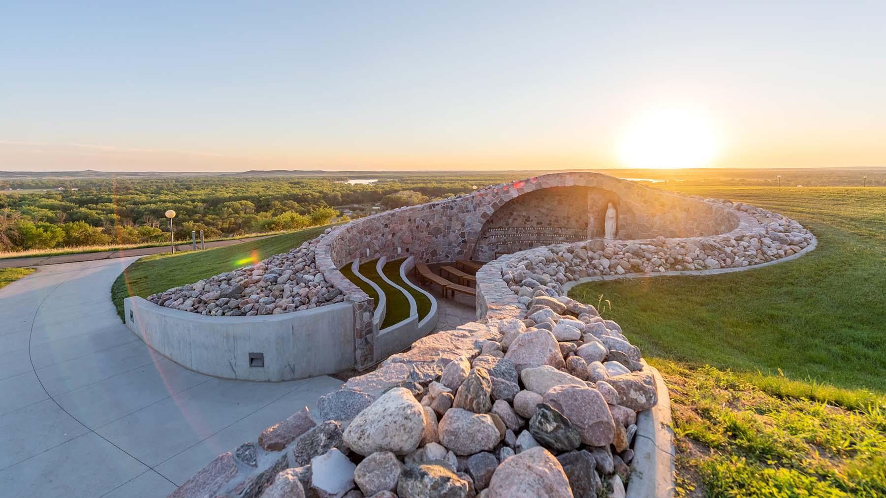 A view of the Grotto with the sun setting over the horizon and a view of Bismarck North Dakota and the Missouri River in the background.