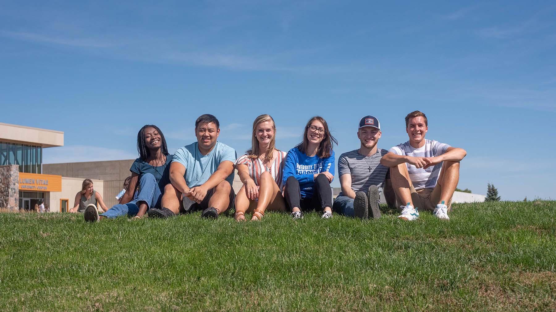 Diverse group of students sitting in grass outside the Lumen Vitae University Center