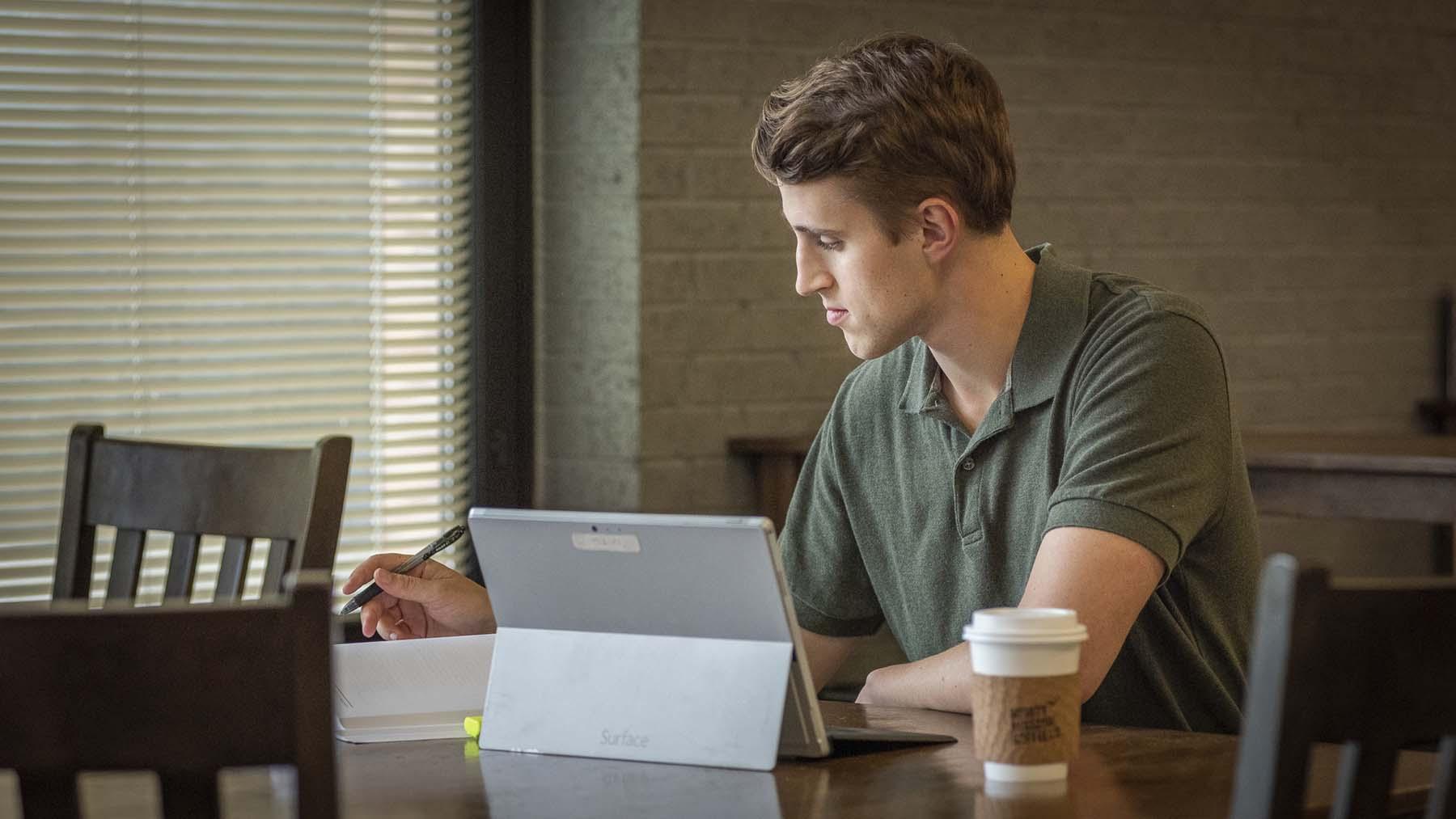Young man studying with laptop open on table in coffee shop