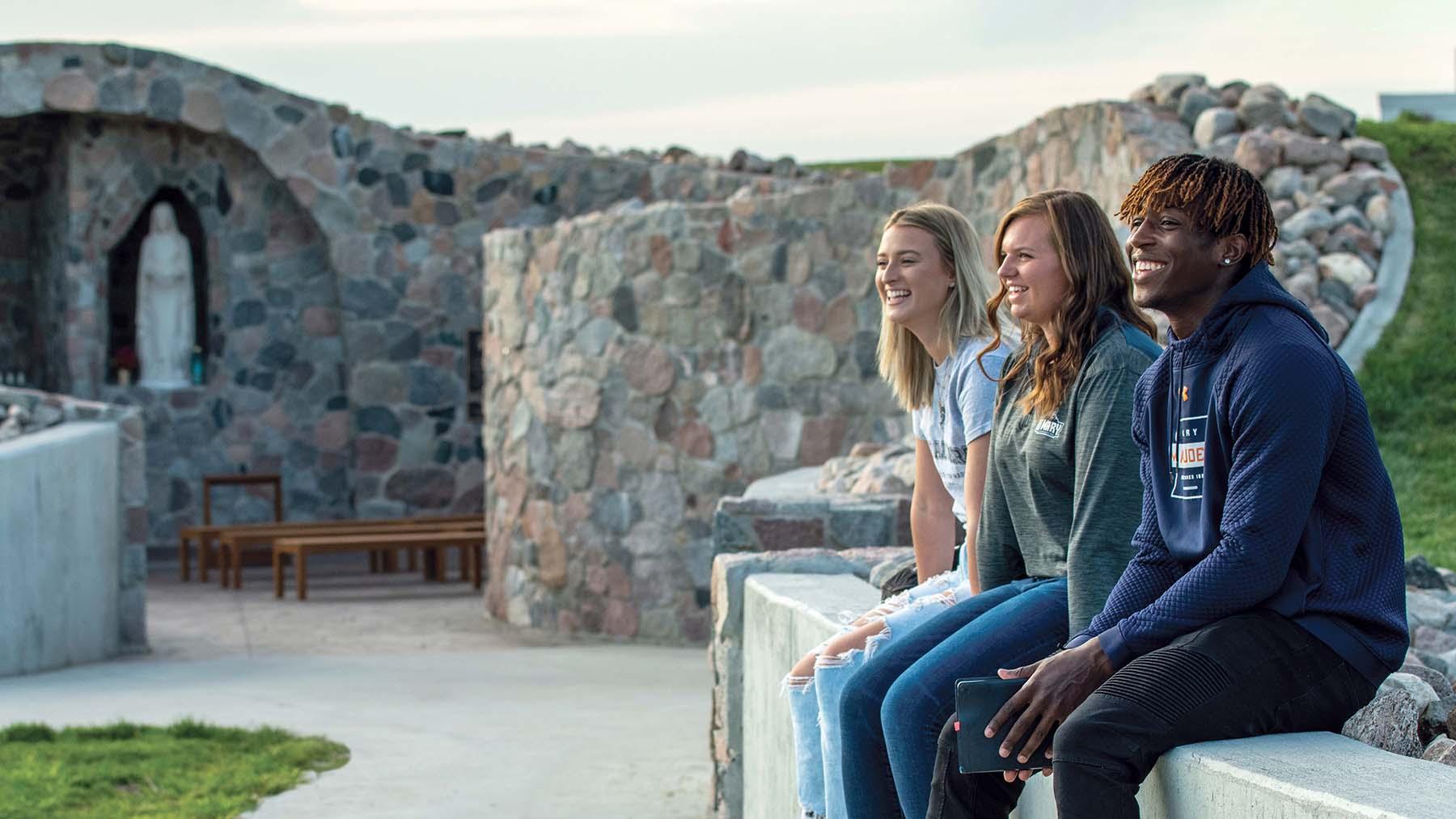 Smiling students sitting on wall outside of grotto