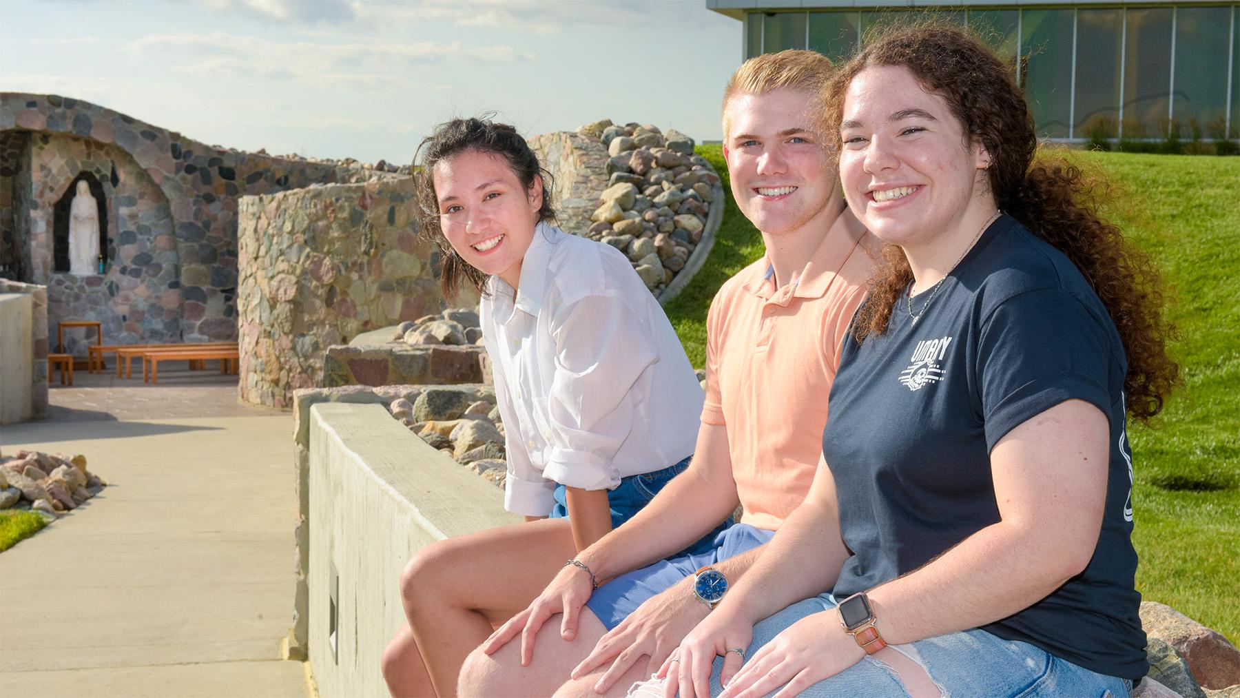 Smiling students sitting on wall outside of grotto